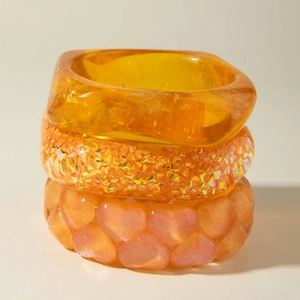 Three-piece stackable orange resin bracelets featuring amber translucent and glitter textures