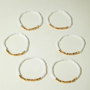 Detail eines sechsteiligen Perlenarmband-Sets mit weißen und goldenen Harzperlen