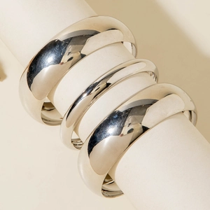 Close-up of three polished silver bangles in varying widths on a white display stand