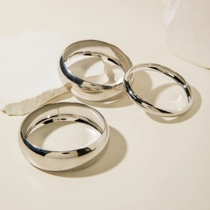 Detailed view of three polished silver bangle bracelets with different widths on white stone