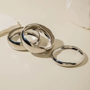 Three-piece polished silver metal bangles set on stone background minimalist jewelry