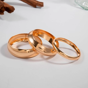 Detailed view of three-piece set of gold polished metal bracelets with glossy mirror finish