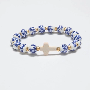 Detail of beaded bracelet with blue floral ceramic beads, gold spacers, and a white cross