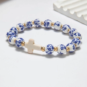 Blue and white ceramic bead bracelet with golden accents and cross charm on grey background