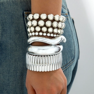 Stacked silver chunky bead bracelets and textured metallic bangles on a denim background
