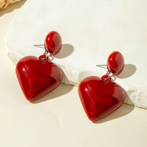 Polished red heart drop earrings with round bead studs on a white marble surface