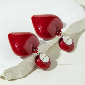 Detail view of glossy deep red heart pendant earrings on white textured stone background