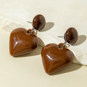 Detailed view of large dark brown polished resin heart pendant earrings on stone surface