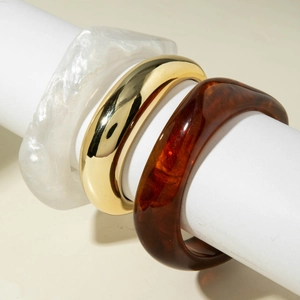 Detail of three stacked bracelets featuring gold metal, pearl white and amber resin
