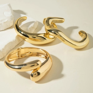 Detailed view of three minimalist polished gold bangles with sculptural organic shapes