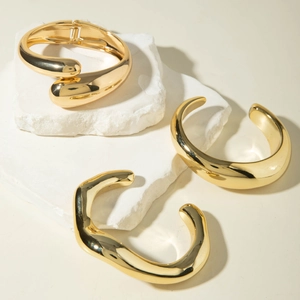 Detailed view of three minimalist polished gold geometric bracelets on white stones