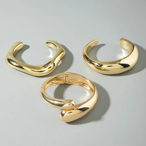 Detailed view of three chunky gold polished geometric open bangles on flat background