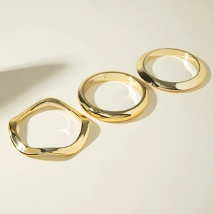 Detail of three minimalist polished gold bangles with irregular wave and smooth geometric designs