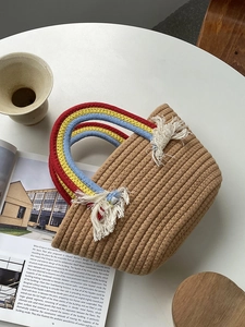 Detalle de bolso tejido a mano con asas de cuerda arcoíris y borlas blancas decorativas