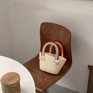Detalle del bolso tejido beige con asas de arcoíris y borlas blancas sobre silla