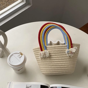 Primer plano del bolso de paja trenzada crema con asa de arcoíris y detalles de borlas