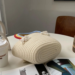 Detalle de bolso tejido a mano con asa de flecos de arcoíris sobre una mesa blanca lisa