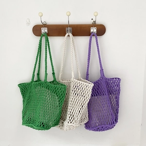 Detail of three handmade macrame tote bags in green, beige and purple hanging on a hook