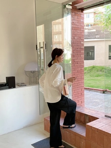 Détail d'une chemise blanche à manches longues et d'un pantalon large noir sur un modèle