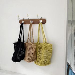 Detail of woven mesh tote bags in black, khaki, and green hanging on wooden hooks