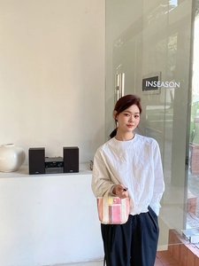 Photo lifestyle d'une femme avec un sac cabas tissé à rayures et un haut blanc plissé