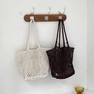 Detail of handmade woven hollow tote bags in beige and brown hanging on a wooden rack