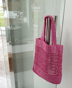 Detalle de bolso de playa fucsia de malla tejida a mano colgado del pomo de una puerta