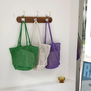 Detail of three colorful handmade hollow woven bags hanging on wooden hooks in summer style