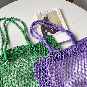 Detail of green and purple handmade woven tote bags with hollow knot texture on a white table