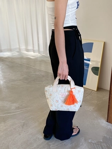 Détail d'un sac à lunch matelassé fleuri avec pompon orange et fermeture éclair