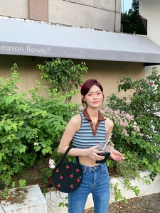Outdoor view of a woman carrying a black woven cherry handbag with a summer outfit