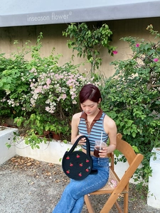 Detail of round black woven cotton bag with embroidered red cherry motifs and handle