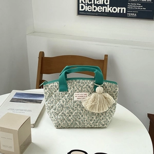 Sac à déjeuner matelassé à fleurs avec anses vertes et gland décoratif sur table