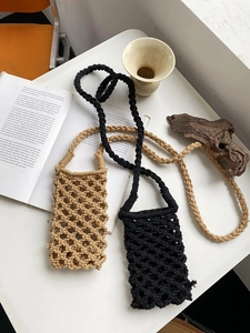 Detail of woven mesh phone bags in khaki and black with braided straps on white desk