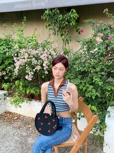 Close-up of a black woven cherry tote bag with red embroidery in a summer garden setting