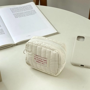 Macro shot of quilted cream storage bag with red text label on a minimalist desk