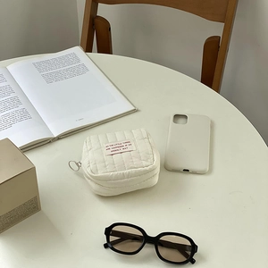 Detailed view of a white quilted mini storage pouch with a large ring zipper pull on a table
