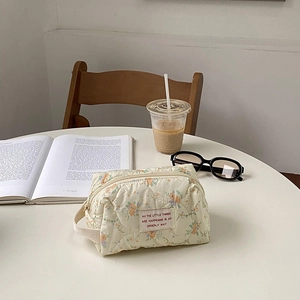 Quilted floral makeup bag with side handle shown next to coffee and sunglasses