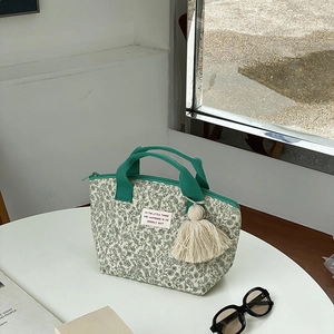 Détail du sac à lunch matelassé à fleurs avec poignées vertes et pompon sur table blanche