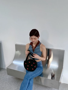 Detail of a black round woven bag with cherry embroidery held by a model on a bench
