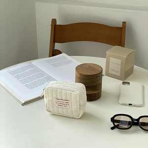 Detailed view of cream quilted mini pouch with red label on a minimalist desk setup
