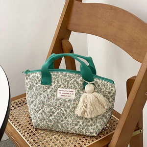Sac à déjeuner matelassé à fleurs avec poignées vertes et gland sur fond osier