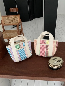Détail de sacs fourre-tout tissés à rayures colorées avec anses en ruban crème sur bois