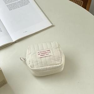 Detailed macro of a quilted cream makeup bag with red lettering on a desk