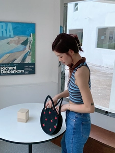 Black woven cherry handbag shown with a striped knit crop top and denim jeans