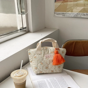 Détail d'un sac bento matelassé à fleurs avec pompon orange et poignées tissées