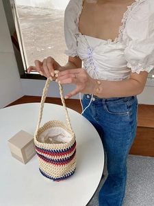 Close-up of handwoven straw bucket bag with red and blue stripes and drawstring closure