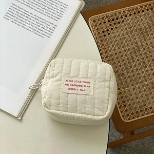Quilted cream cosmetic bag with textile label on an open book and wooden chair