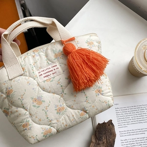 Détail du sac à lunch matelassé à fleurs avec poignées beige et pompon orange décoratif