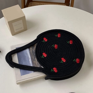 Detailed view of black round woven cotton bag with red cherry embroidery and long strap
